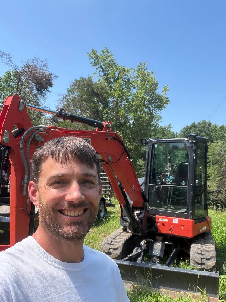Blake, founder of Carbide & Dirt, on a job site in front of his tracked excavator.